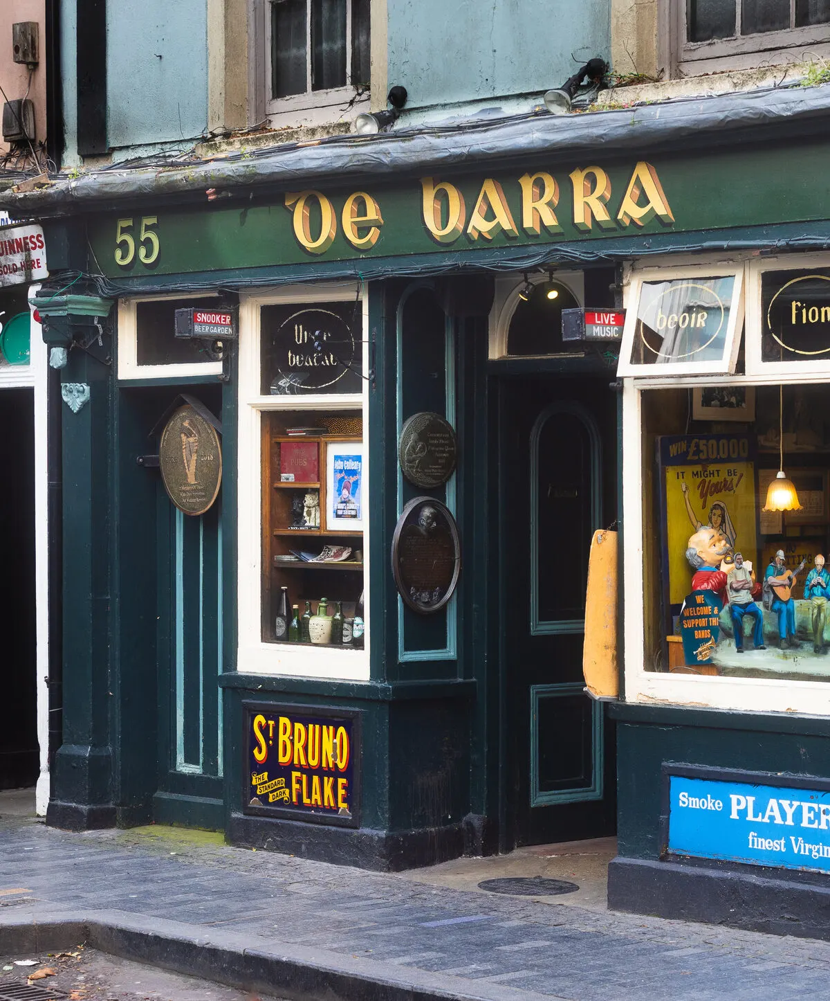 The dark green and gold shopfront of De Barra's in Clonakilty, its name in Gaelic script above the lit window display