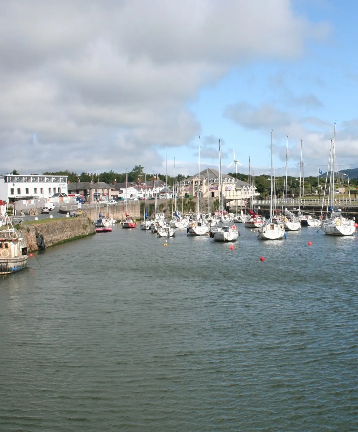 Courtown harbour, yachts and small boats moored along the basin inside its stone quay wall, with the village and lifeboat house behind