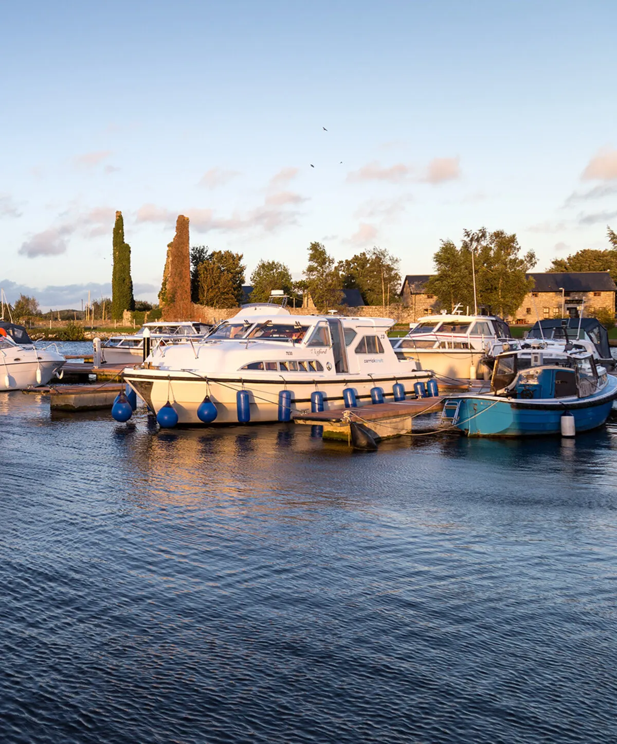 Cruisers moored along the pontoons at Dromineer harbour on Lough Derg in low evening light, with the stone buildings of the shore behind
