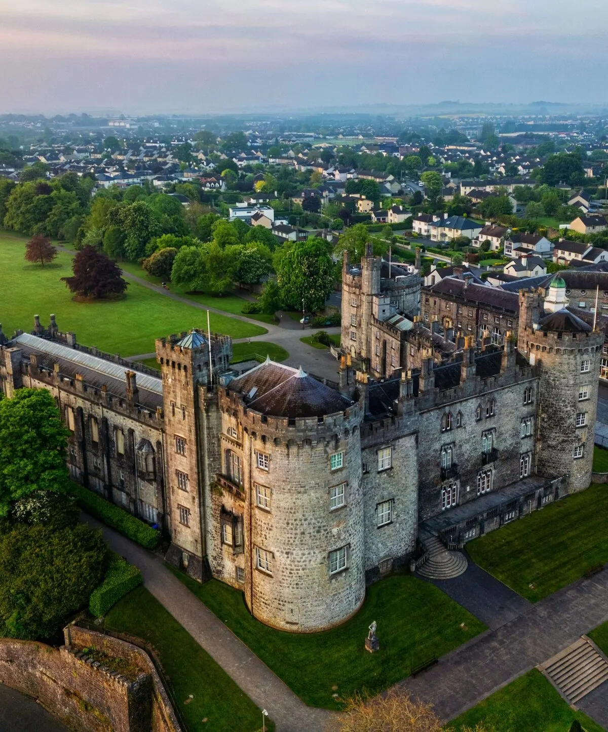 Kilkenny Castle seen from above at dawn, with the rooftops of the city and the hills beyond it