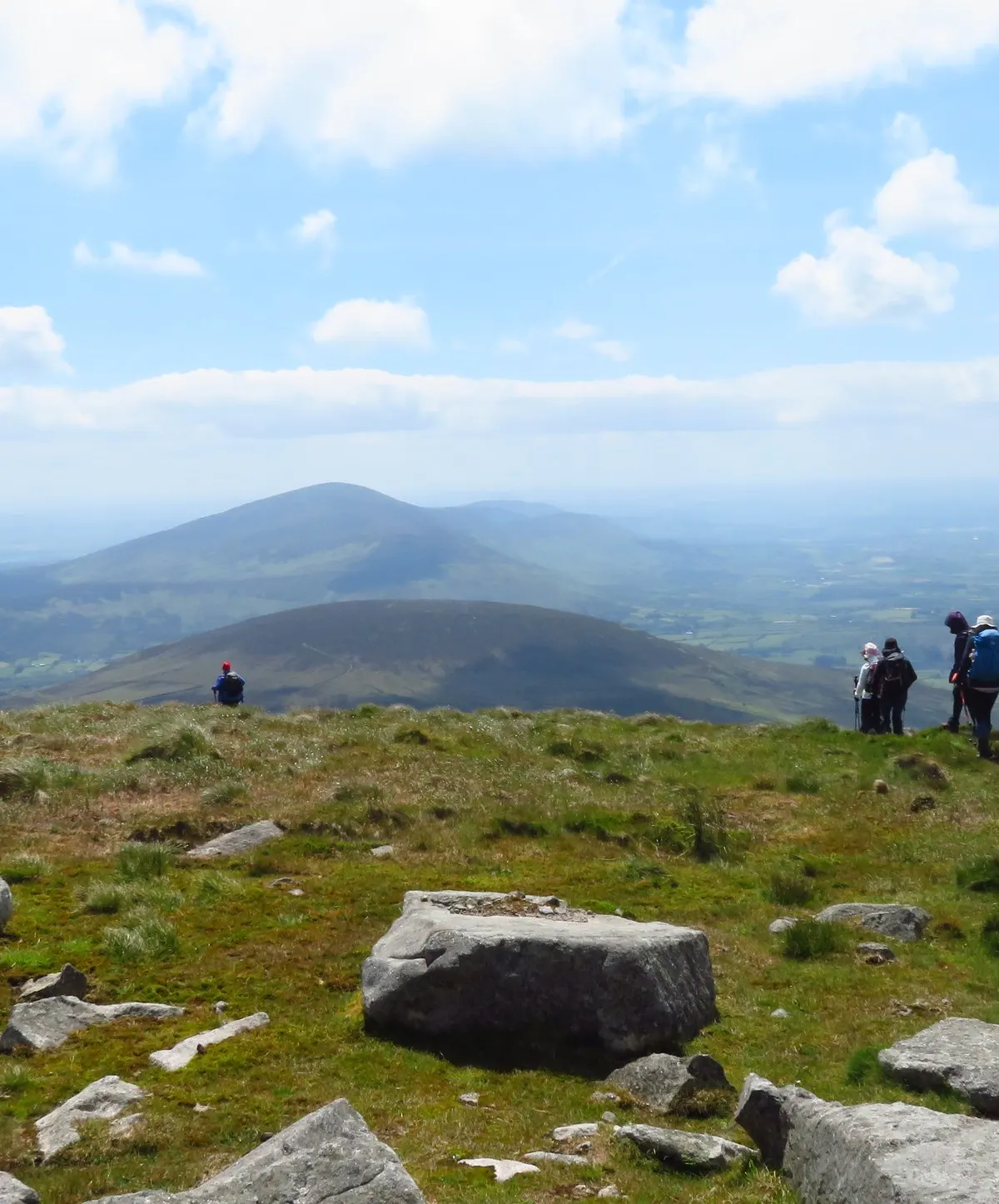 Walkers on the summit of Mount Leinster looking south along the ridge towards Blackstairs Mountain, with granite outcrops in the foreground and farmland below