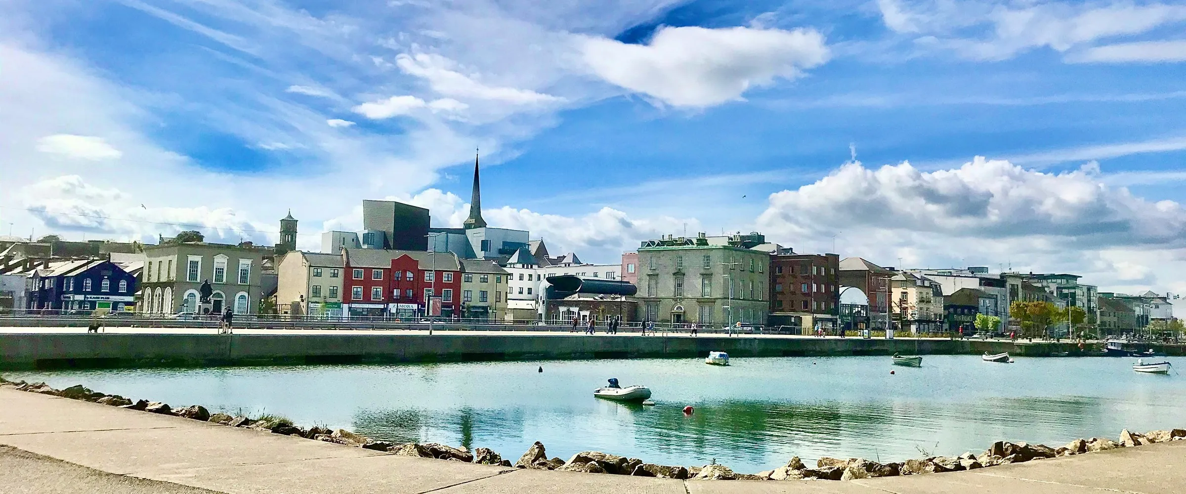 The quay front of Wexford town seen across the harbour, its painted terraces and church spire in a line above the water, with the National Opera House among them